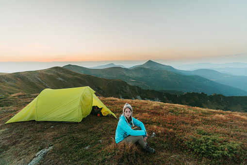 Scenic view of  young Caucasian woman sitting near the tent in mountains