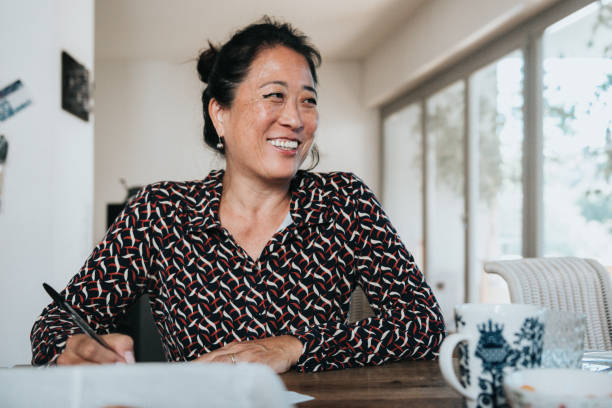 verticale de femme élégante de sourire travaillant l’écriture avec le stylo à la table en bois - women asian ethnicity business mature adult photos et images de collection