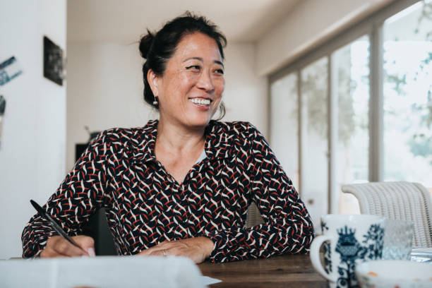 portrait of smiling elegant woman working writing with pen at wooden table - shirt ethnic ethnicity one person imagens e fotografias de stock