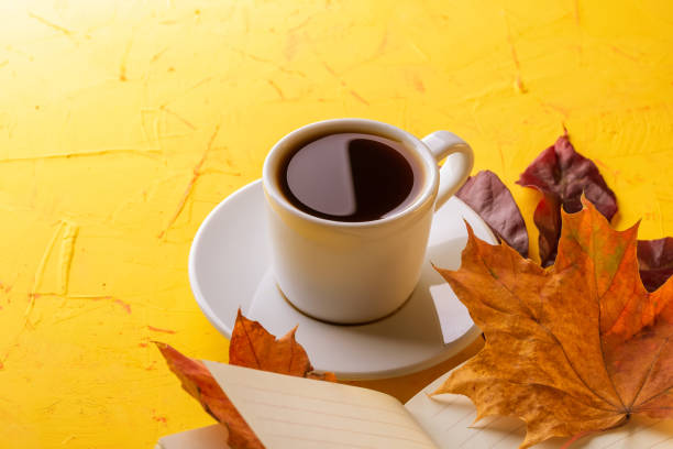 istock Autumn concept. A cup of espresso, a blank notepad and fall foliage on a yellow concrete table. Copy space 1278798772