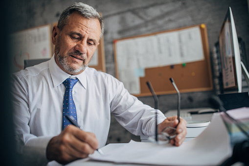 Smiling mature business leader signing a document in his office