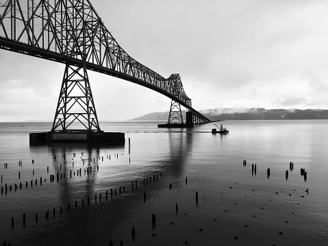 Fishing boat on the Columbia River passing under the Astoria Megler Bridge on a cloudy morning. From the Astoria, Oregon, USA side.