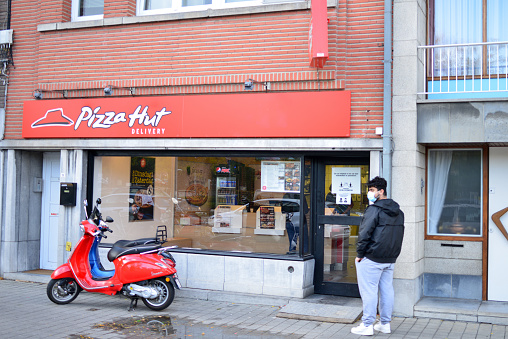 Leuven, Vlaams-Brabant, Belgium - October 6, 2020: exterior building pizza Hut Delivery. Vespa and young adult man with safety mask in front of store.