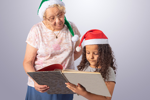 Elderly woman and child with Christmas hat reading a book, gray gradient background, selective focus.