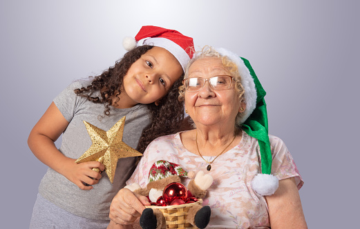 Elderly woman and child with Christmas hat and Christmas ornaments in hands, gray gradient background, selective focus.