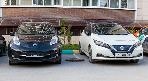 Novosibirsk, Russia - 08.21.2020: Two electric cars of Japanese production Nissan Leaf on the asphalt in the city near a multi-storey building. Environmentally friendly transport.