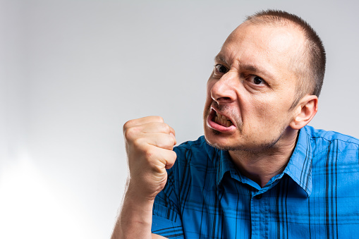 Angry aggressive man shouting out loud with ferocious expression. Angry man. Man isolated showing fist to camera, aggressive facial expression.