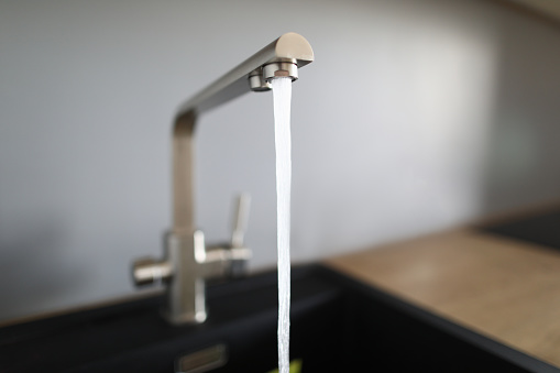 Close-up of kitchen faucet and water pressure in new modern apartment. Cropped picture of domestic appliances. Equipment to wash hands or dish. Renovation and moving day concept