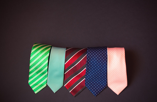 Rolled stylish multi colored neckties on dark background. Top view, copy space.