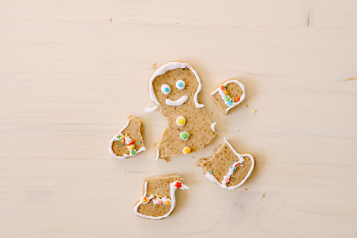Gingerbread man with severed legs and arms. The limbs of the cookie are separated from the body. Christmas gingerbread on a white wooden background. High quality photo