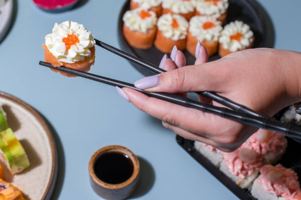 sushi auf blauem hintergrund. nahaufnahme der hand mit essstäbchen - chopsticks soybean japanese cuisine blue stock-fotos und bilder