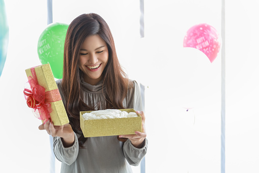 Happy New Year, Christmas and Holiday Seasonal Concept. Portrait of young asian woman holding and opening a beautiful gift box with copy space for text