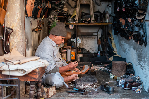 Jamnagar, Gujarat, India - December 2018: An Indian cobbler working on shoe repair in his roadside shop.