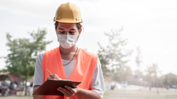 istock Young male construction worker with yellow helmet and face mask taking notes at construction site. New normality after covid-19 outbreak. 1278837490