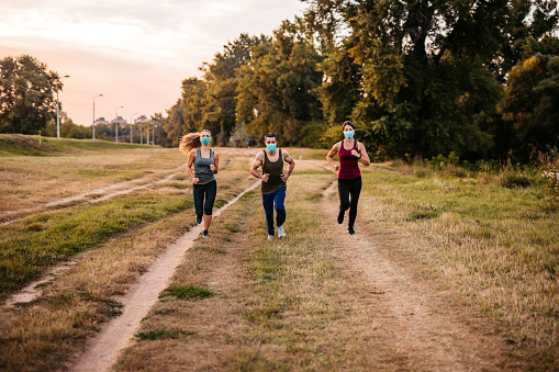 Three young active friends jogging together with protective face masks on.