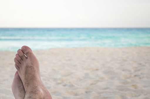 Great vacation concept, male feet on a beach chair pointing to the turquoise Caribbean sea.