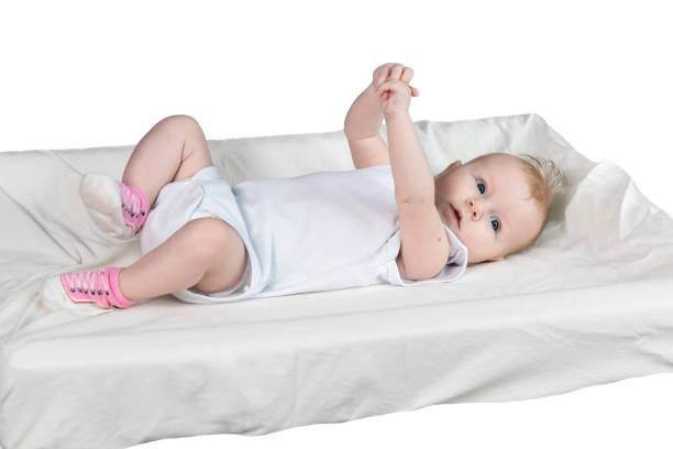 白い服を着た生後4ヶ月の赤ちゃんが、おとりテーブルの上に仰向けに横たわっている。腕と脚が上がっています。赤ちゃんは機嫌がいい - child lying on back setting the table clothing ストックフォトと画像
