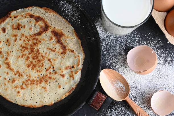 istock Hot pancake in black pan on black table with flour, milk and eggs 1278846035