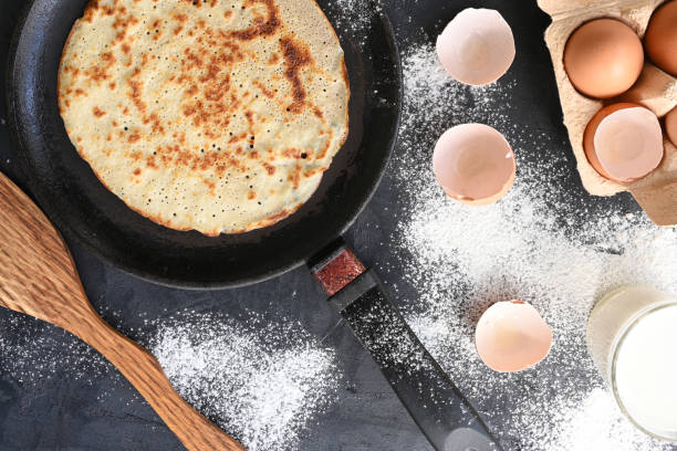 istock Hot pancake in black pan on black table with flour, milk and eggs 1278846544