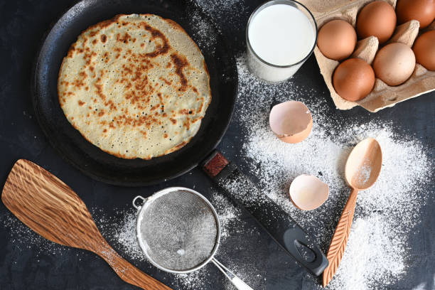 istock Hot pancake in black pan on black table with flour, milk and eggs 1278846551