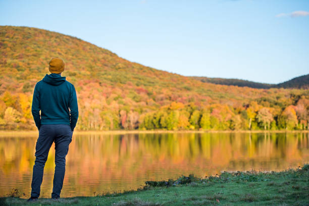 Young man surrounded by vibrant autumn colors. Young peaceful man out in nature alone reflecting on a vibrant autumn scene. hudson valley stock pictures, royalty-free photos & images