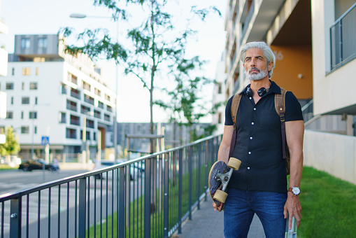 Front view portrait of mature man with skateboard outdoors in city, going back to work.