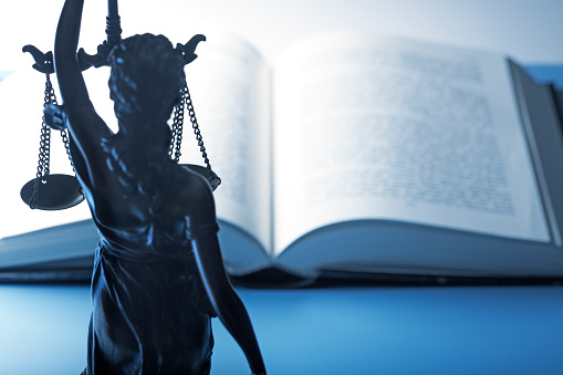 Lady Justice in front of an open law book out of focus in the background.