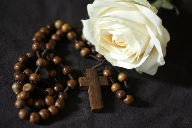 Wooden rosary beads and a single white rose on dark background.