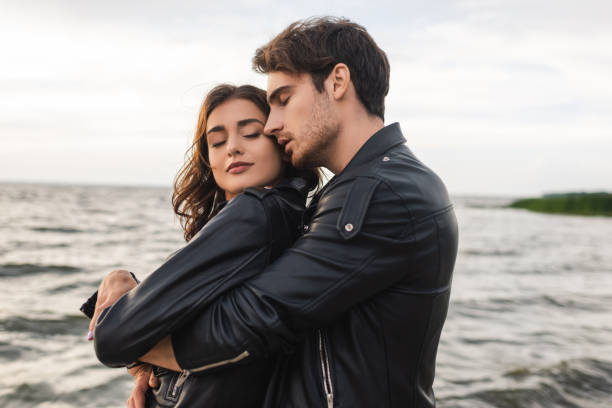 istock Side view of man embracing girlfriend in leather jacket near sea 1278856310