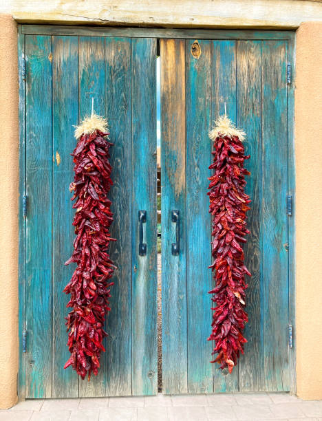 new mexico: long chili pepper ristras auf alten türkisfarbenen türen - wreath chili pepper pepper ristra stock-fotos und bilder