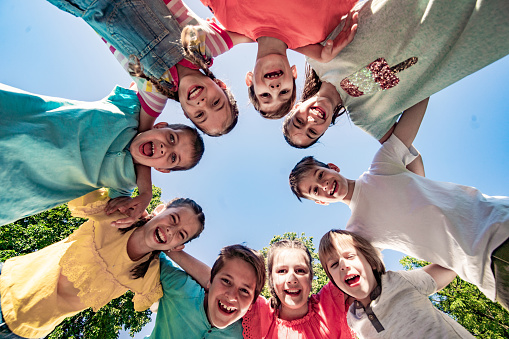 Group of happy multiracial teenagers, smiling friends wearing colorful t shirts embracing, looking at camera on street. Positive school boys and girls standing together. Friendship, vacation, summer