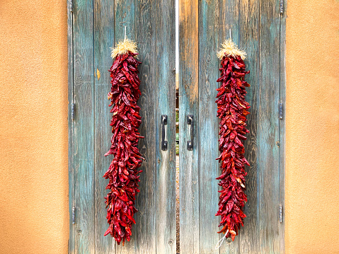 New Mexico: Long Chili Pepper Ristras on Old Turquoise Doors. Adobe wall background. Shot in Santa Fe.