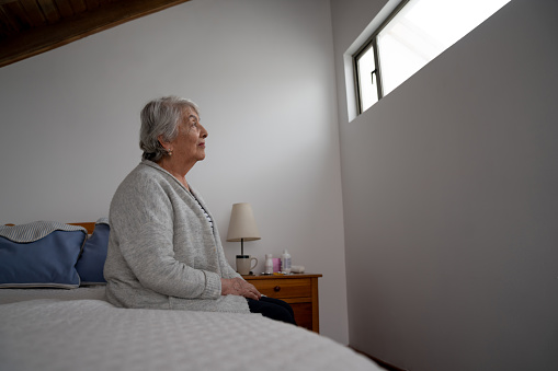 Thoughtful Latin American senior woman sitting on her bed at a nursing home â aging process concepts