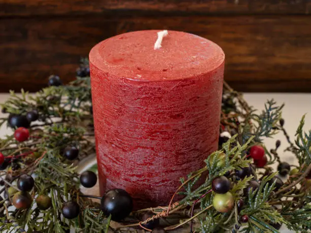 Photo of A red Christmas candle surrounded by cedar boughs and berries