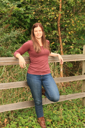 A woman leaning on a rustic fence and looking at the camera.