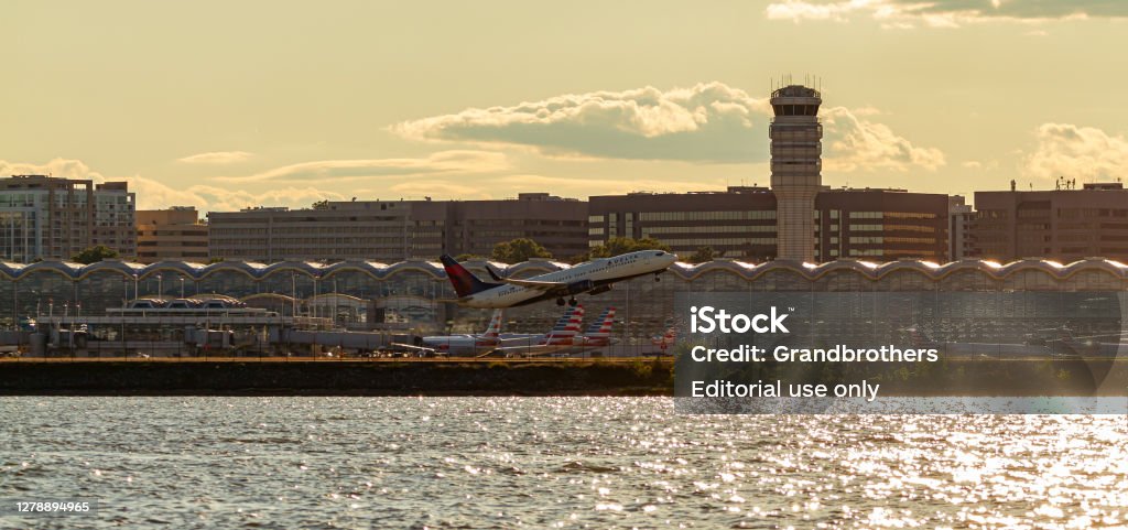 Panoramic view of Ronald Reagan National Airport across Potomac River at sunset. i Washington DC, USA 10/03/2020: Panoramic view of Ronald Reagan National Airport across Potomac River at sunset. image features the tower, terminals, parked planes and a Delta Airline plane taking off. Aerospace Industry Stock Photo