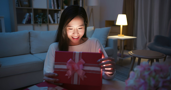 surprised asian young woman opening her christmas present box at home happily