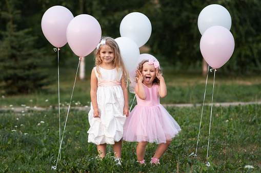 Two little girls in pink and white dressses with balloons walking in the park
