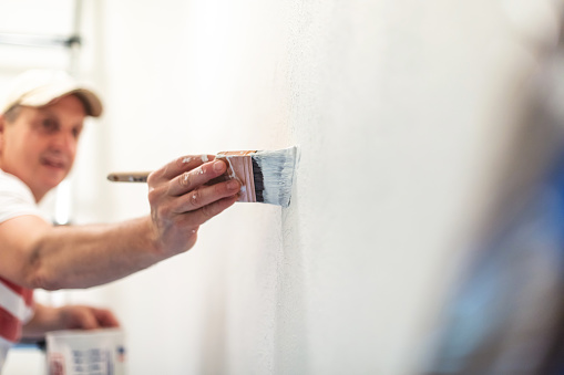 In Western Colorado Mature Adult Male Using Paint Brush to Spread White Wall Paint; Private Residence Remodel and Updates Photo Series with Matching 4K Video Available (Shot with Canon 5DS 50.6mp photos professionally retouched - Lightroom / Photoshop - original size 5792 x 8688 downsampled as needed for clarity and select focus used for dramatic effect)