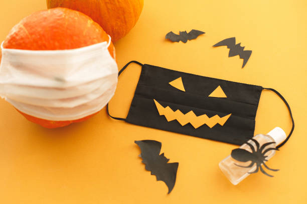 istock Halloween 2020 safe creative celebration. Evil face mask, pumpkin in mask, disinfection gel bottle 1278906518