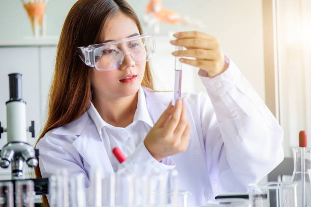 attraktive junge asiatische wissenschaftlerin labortechnikerassistentin, die die probe im reagenzglas im labor analysiert. medizinisches, pharmazeutisches und wissenschaftliches forschungs- und entwicklungskonzept. - scientist research test tube lab coat stock-fotos und bilder