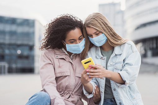 Cute girls using smartphone on a city street. People, technology, friendship,  mobile app, city life, lifestyle, social media, epidemic, pandemic, corona virus protection, healthy lifestyle concept