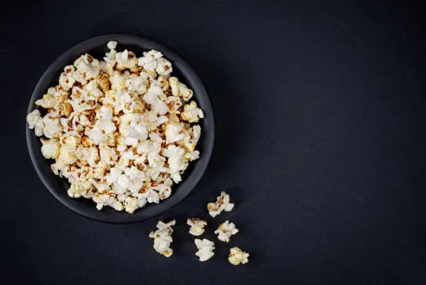 Photo of Scattered salted popcorn in a bowl  on black background with copy space. Homemade Popcorn  Top view. 