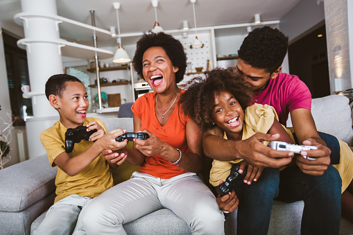 African American family at home sitting in sofa couch and playing video games together