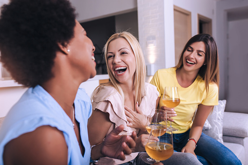 Happy young female friends with wine on sofa at home.