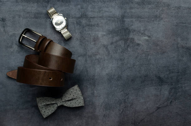 Top view of accessories for man on the grey surface.Watch, leather belt, bow tie.Empty space