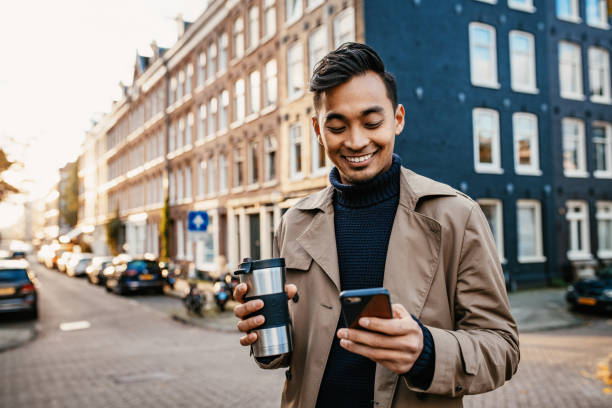 Asian businessman using smart phone and drinking coffee from reusable cup