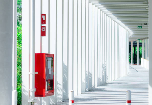 istock Empty walkway between buildings in the morning with shade of sunlight through space between white pole. Red fire extinguisher installed on concrete pole for safety. Modern architecture of corridor. 1278927670