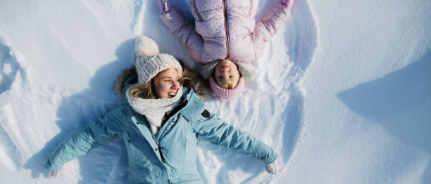 вид сверху портрет веселой мамы с маленькой дочкой, лежащей в снегу в зимней природе. - offspring child lying on back parent стоковые фото и изображения