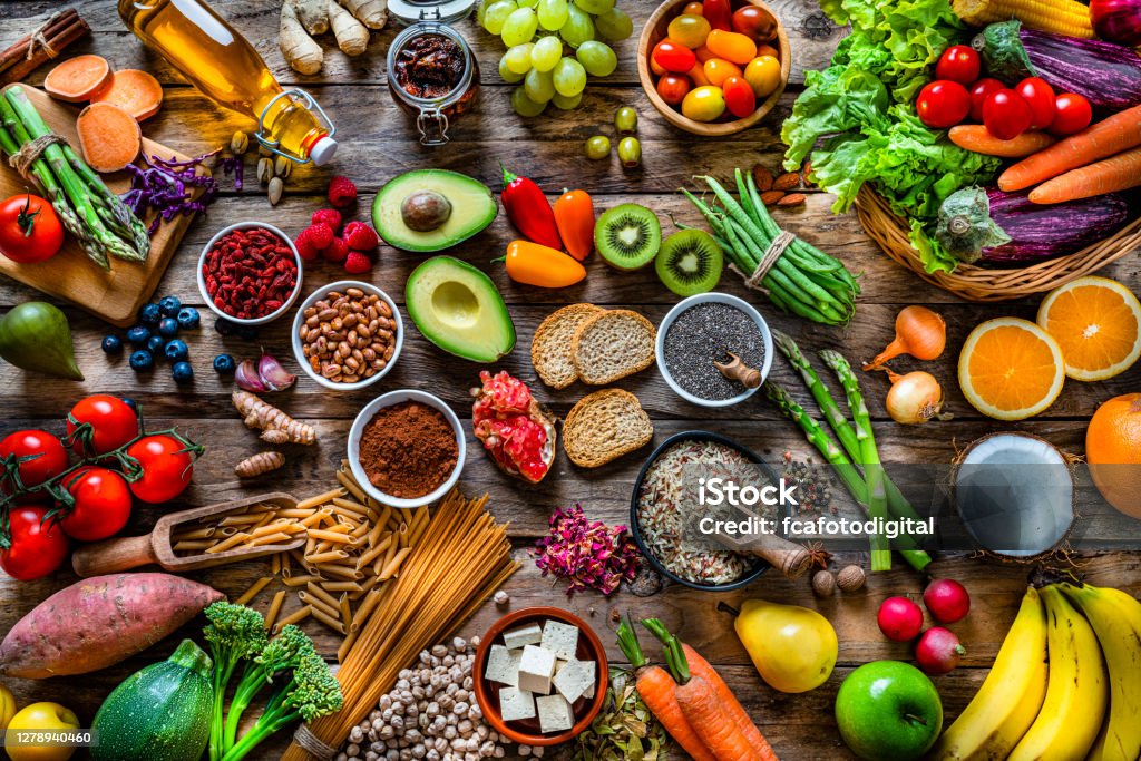 Vegan food backgrounds: large group of fruits, vegetables, cereals and spices shot from above Vegan food backgrounds: large group of multicolored fresh fruits, vegetables, cereals and spices shot from above on wooden background. The composition includes green apple, kiwi, pear, pomegranate, orange, coconut, banana, grape, berries, ginger, almonds, pistachio, olive oil, olives, goji berries, chia seeds, pinto beans, nutmeg, rosemary, radish, tomatoes, carrot, kale, avocado, onion, rice, cocoa powder, sweet potato, wholegrain pasta, tofu, lettuce, corn, broccoli, pepper, asparagus, green beans, among others. High resolution 42Mp studio digital capture taken with SONY A7rII and Zeiss Batis 40mm F2.0 CF lens Healthy Eating Stock Photo